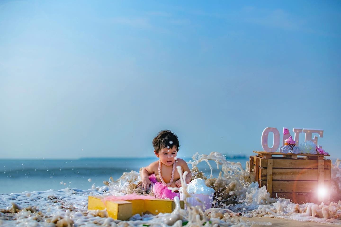 A baby splashing in ocean waves at a beach birthday shoot — the kind of joyful moment clients star as a favorite in their RawDrive gallery.